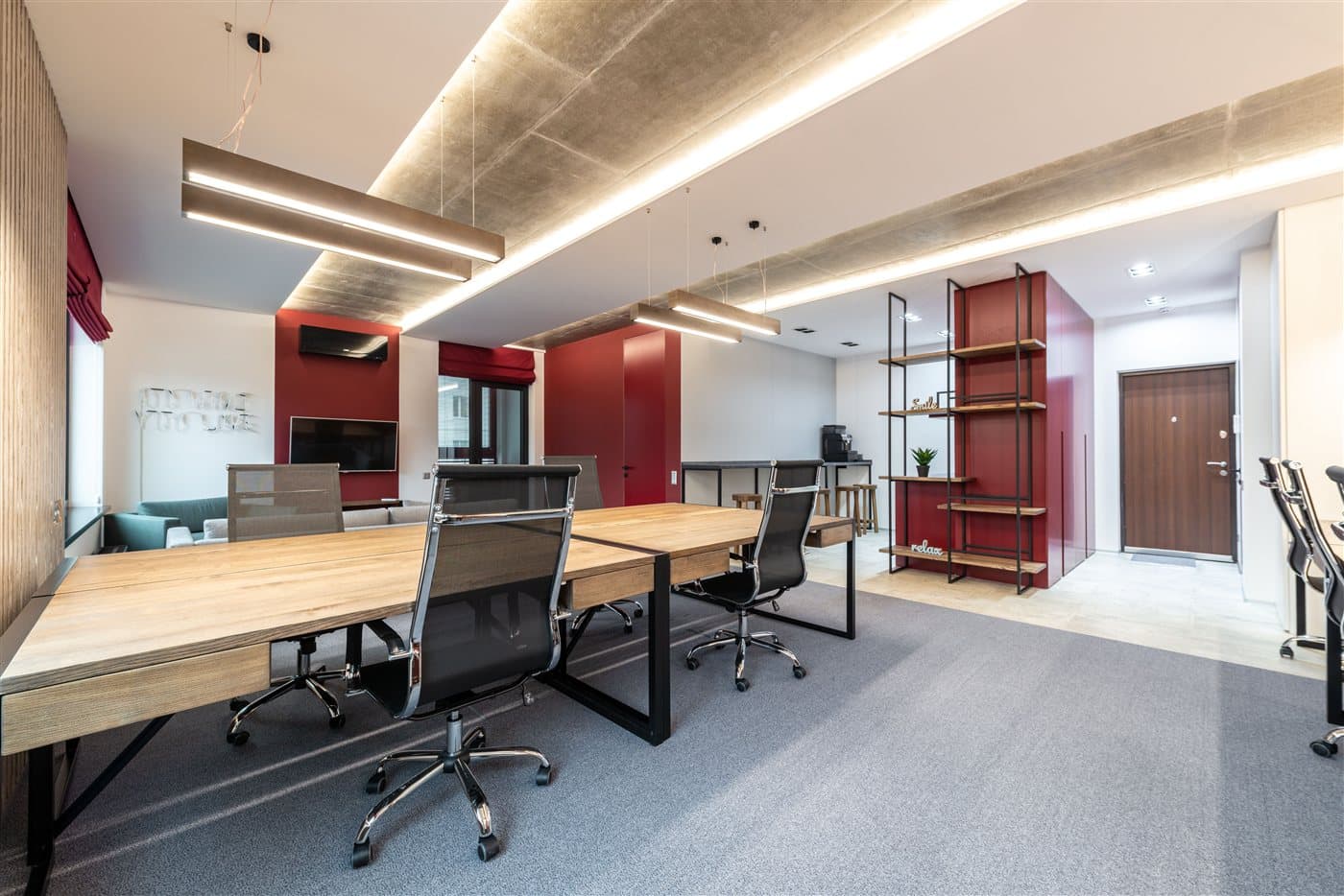 Offenes Büro mit Holztischen, Lichtbändern an der Decke und roten Akzentwänden