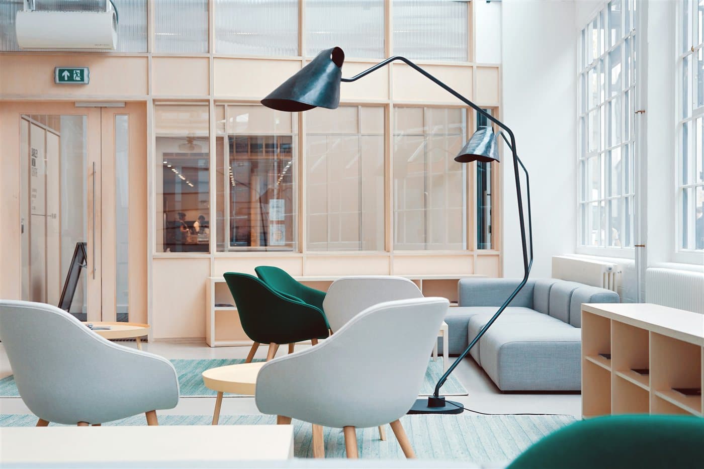 Heller Loungebereich mit Sesseln, modularem Sofa, Stehleuchte und Holzregalen